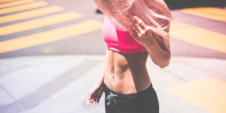 woman with straight blonde hair wearing activewear, looking down at her abs